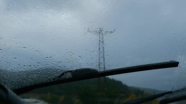 巨大な電気ポストと曇りの空の背景と雨の日の間にフロントガラスワイパーの遅い動きビデオ — ストック動画