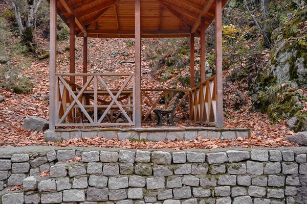 アーバーと秋 木製のアーバー 石の壁に秋の色の多くの乾燥葉で覆われたベンチ — ストック写真