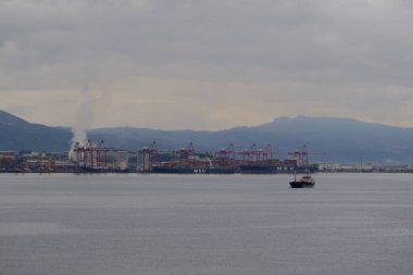 Gökyüzü bulutlu, mücevher ve büyük fabrikalar ve deniz teknesi.