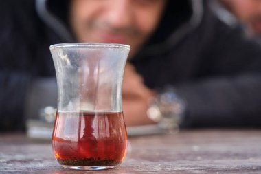 Geleneksel Türk çayı, geleneksel ince beli cam bardakta bulanık gülümseyen adam fotoğrafı çay bardağının arkasında..