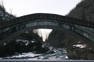 Kışın taş köprünün alçak açılı görüntüsü. Taş köprünün altındaki nehir ve kar kışı