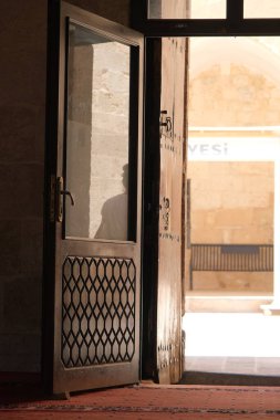 Ancient wooden gate, engraved door, gate opening inside the mosque in Mardin, hot summer day, silhouette of people reflection on the door.