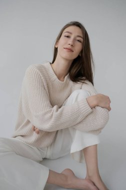 Tarafsız gri arka planda bej kazaklı, beyaz bisiklet pantolonlu havalı kız. Yumuşak ışık, tek renkli resim. İyi titreşimler, olumlu duygular. Uzun ve ince Avrupa modeli iyi durumda..