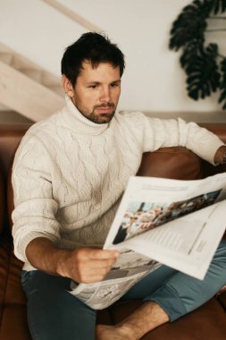 Dairesinde Avrupalı bir adam var. Oturma odasında, kanepede oturuyor. İş gazetesi okuyorum. Beyaz kazak, kot pantolon. Bronz ten. Siyah gözler ve saçlar. Sakal. Açık renkli iç mekan.