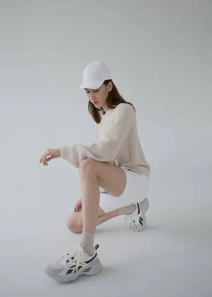 Tarafsız gri arka planda bej kazaklı, beyaz bisiklet pantolonlu havalı kız. Yumuşak ışık, tek renkli resim. İyi titreşimler, olumlu duygular. Uzun ve ince Avrupa modeli iyi durumda..