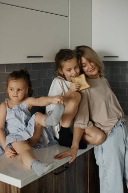 Mutfakta iki güzel kızı olan genç ve güzel bir anne. Mutlu aile kahvaltıları. Şık bir iç mekan. İyi ilişkiler. Komik çocuklar. Sevgi ve ilgi. Avrupalılar. Canlı ve doğal görüntü