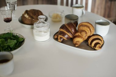 Beyaz masada lezzetli ve sağlıklı bir kahvaltı. Kruvasan, süt, bal, ekmek. Avrupa yaşam tarzı. Akdeniz yemekleri. Şık yemekler. Modern iç mekan. Taze fırın. Ispanak. Çay ve kahve. Taze meyve suyu