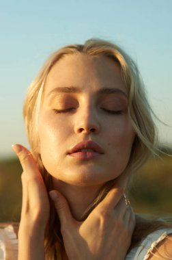 Beyaz romantik elbiseli, yaz mevsiminde muhteşem bir genç kadın. Sarı çimenler, mavi gökyüzü. Güneşli bir gün. Büyük güzel gözleri ve güzel dudakları olan sarışın bir manken. Sakin ve dengeli. Şık görünüş.  