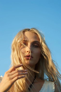 Beyaz romantik elbiseli, yaz mevsiminde muhteşem bir genç kadın. Sarı çimenler, mavi gökyüzü. Güneşli bir gün. Büyük güzel gözleri ve güzel dudakları olan sarışın bir manken. Sakin ve dengeli. Şık görünüş.  