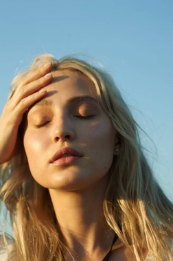 Beyaz romantik elbiseli, yaz mevsiminde muhteşem bir genç kadın. Sarı çimenler, mavi gökyüzü. Güneşli bir gün. Büyük güzel gözleri ve güzel dudakları olan sarışın bir manken. Sakin ve dengeli. Şık görünüş.  