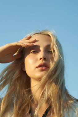 Beyaz romantik elbiseli, yaz mevsiminde muhteşem bir genç kadın. Sarı çimenler, mavi gökyüzü. Güneşli bir gün. Büyük güzel gözleri ve güzel dudakları olan sarışın bir manken. Sakin ve dengeli. Şık görünüş.  