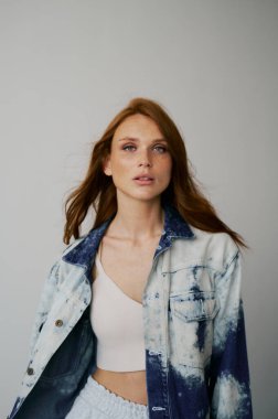 Kızıl saçlı, mavi gözlü ve uzun dalgalı kızıl saçlı güzel bir manken. Şehvetli ve çekici bir kadın. Çiller. Tarafsız bir arkaplan. Mükemmel kalite. Yumuşak ışık. Kot ceket. Güzel kirpikleri, büyük dudakları, güzel gözleri var.