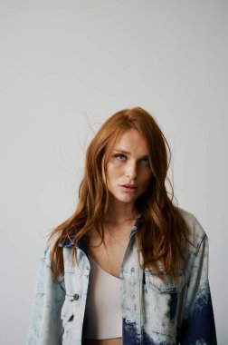 Kızıl saçlı, mavi gözlü ve uzun dalgalı kızıl saçlı güzel bir manken. Şehvetli ve çekici bir kadın. Çiller. Tarafsız bir arkaplan. Mükemmel kalite. Yumuşak ışık. Kot ceket. Güzel kirpikleri, büyük dudakları, güzel gözleri var.