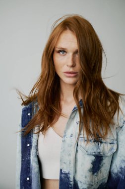 Kızıl saçlı, mavi gözlü ve uzun dalgalı kızıl saçlı güzel bir manken. Şehvetli ve çekici bir kadın. Çiller. Tarafsız bir arkaplan. Mükemmel kalite. Yumuşak ışık. Kot ceket. Güzel kirpikleri, büyük dudakları, güzel gözleri var.
