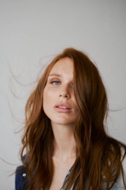 Kızıl saçlı, mavi gözlü ve uzun dalgalı kızıl saçlı güzel bir manken. Şehvetli ve çekici bir kadın. Çiller. Tarafsız bir arkaplan. Mükemmel kalite. Yumuşak ışık. Kot ceket. Güzel kirpikleri, büyük dudakları, güzel gözleri var.