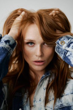 Kızıl saçlı, mavi gözlü ve uzun dalgalı kızıl saçlı güzel bir manken. Şehvetli ve çekici bir kadın. Çiller. Tarafsız bir arkaplan. Mükemmel kalite. Yumuşak ışık. Kot ceket. Güzel kirpikleri, büyük dudakları, güzel gözleri var.