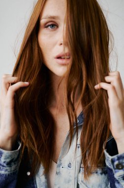 Kızıl saçlı, mavi gözlü ve uzun dalgalı kızıl saçlı güzel bir manken. Şehvetli ve çekici bir kadın. Çiller. Tarafsız bir arkaplan. Mükemmel kalite. Yumuşak ışık. Kot ceket. Güzel kirpikleri, büyük dudakları, güzel gözleri var.