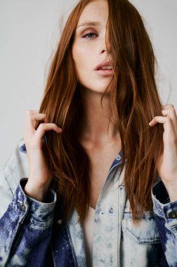 Kızıl saçlı, mavi gözlü ve uzun dalgalı kızıl saçlı güzel bir manken. Şehvetli ve çekici bir kadın. Çiller. Tarafsız bir arkaplan. Mükemmel kalite. Yumuşak ışık. Kot ceket. Güzel kirpikleri, büyük dudakları, güzel gözleri var.