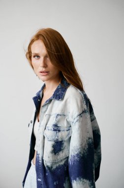 Kızıl saçlı, mavi gözlü ve uzun dalgalı kızıl saçlı güzel bir manken. Şehvetli ve çekici bir kadın. Çiller. Tarafsız bir arkaplan. Mükemmel kalite. Yumuşak ışık. Kot ceket. Güzel kirpikleri, büyük dudakları, güzel gözleri var.