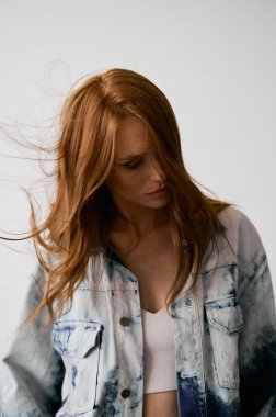 Kızıl saçlı, mavi gözlü ve uzun dalgalı kızıl saçlı güzel bir manken. Şehvetli ve çekici bir kadın. Çiller. Tarafsız bir arkaplan. Mükemmel kalite. Yumuşak ışık. Kot ceket. Güzel kirpikleri, büyük dudakları, güzel gözleri var.