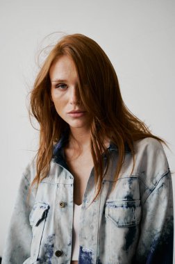 Kızıl saçlı, mavi gözlü ve uzun dalgalı kızıl saçlı güzel bir manken. Şehvetli ve çekici bir kadın. Çiller. Tarafsız bir arkaplan. Mükemmel kalite. Yumuşak ışık. Kot ceket. Güzel kirpikleri, büyük dudakları, güzel gözleri var.