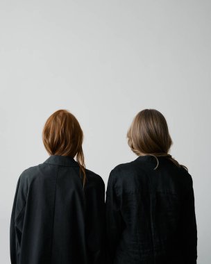 Saç reklamı. Tarafsız arka planda siyah elbiseli iki kızıl kız. Güzel uzun dalgalı saçlar. Oldukça uzun modeller. Doğal güzellik. Minimalizm. Şık, modaya uygun. Yumuşak ışık. Bakım ve onarım. Yüzler yok
