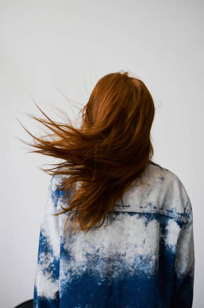 Nice model with red hair, blue eyes and long wavy red hair. Sensual attractive woman. Freckles. Neutral background. Excellent quality. Soft light. Blue jacket. Nice lashes, big lips, beautiful eyes. Back view, no face