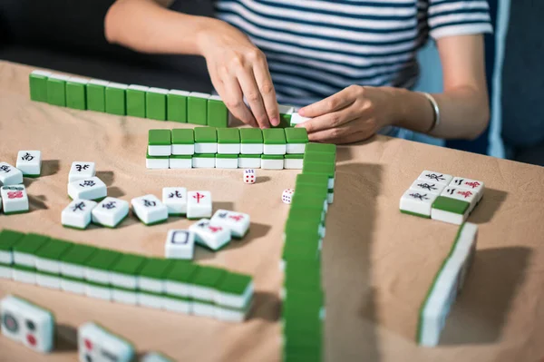 Female friends playing mahjong traditional Chinese board game at home. Translation: Tiles text shows Chinese characters for numbers from 1 to 9 and sides of the world: east, west, north,south