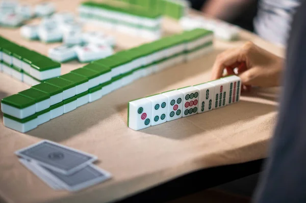 Female friends playing mahjong traditional Chinese board game at home. Translation: Tiles text shows Chinese characters for numbers from 1 to 9 and sides of the world: east, west, north,south
