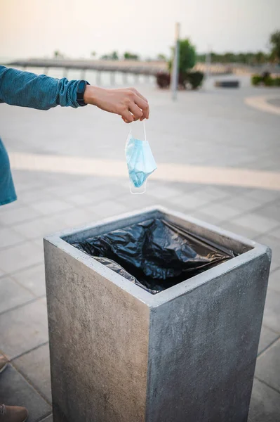 Unrecognizable pregnant woman throwing a used surgical medical face mask in the garbage bin outdoors