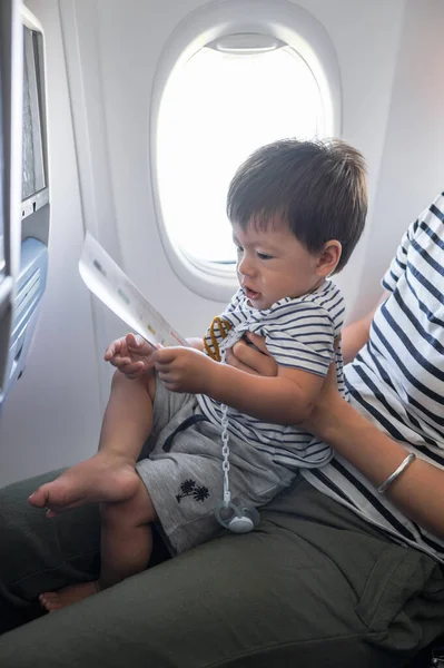 Infant traveling in airplane sitting on its mother lap. One year old baby boy flying in airplane and trying to entertain himself