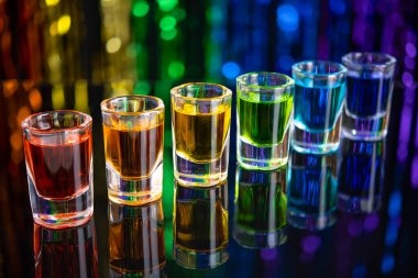 Gökkuşağı içeceği. Bir bardak alkol likörü. Bar tezgahı. Gökkuşağı renkleri. Renkli votka. LGBT Gururu. Gökkuşağı bayrağı, sembol geyler ve lezbiyenler LGBT, LGBTQ. Parti için iyi. Siyah arkaplanda gökkuşağı.