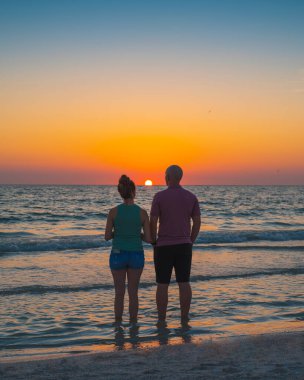 Okyanus batımı. Kumsalda bir çift adam ve kadın. Yaz tatilindeki aile. Güzel, parlak gün batımı. Çift silueti, kız ve erkek..