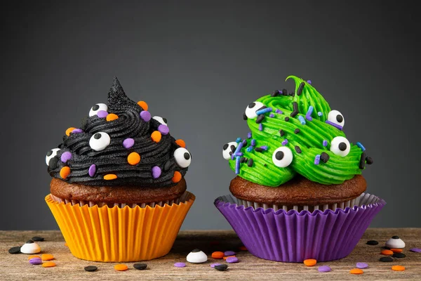 Cupcake on Halloween. Dessert on Halloween party. Chocolate muffin decorated with colored sprinkles, black, green frosting, icing. Cupcakes on dark background and wooden desk. Macro high quality photo