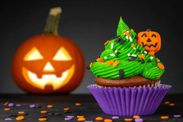 Cupcake on Halloween. Carved pumpkin Jack o lantern. Dessert on Halloween party. Muffin decorated with colored sprinkles, frosting and Icing shaped pumpkin Jack-o-lantern. Cupcakes on dark background