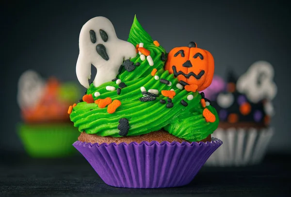 Cupcake on Halloween. Pumpkin Jack o lantern and ghost. Dessert on Halloween party. Muffin decorated with colored sprinkles, frosting and Icing shaped pumpkin Jack-o-lantern. Dark background.