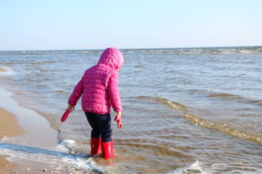 Sonbaharda deniz kenarında oynayan kız çocuğu. Deniz kıyısında güzel bir sonbaharda kırmızı ceketli bir kız. Kontrışık.
