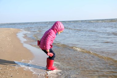 Sonbaharda deniz kenarında oynayan kız çocuğu. Deniz kıyısında güzel bir sonbaharda kırmızı ceketli bir kız. Kontrışık.