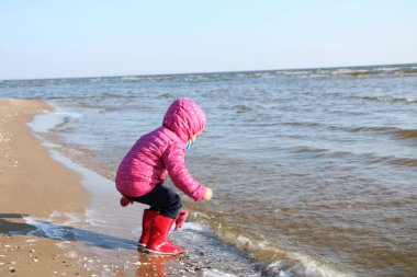 Sonbaharda deniz kenarında oynayan kız çocuğu. Deniz kıyısında güzel bir sonbaharda kırmızı ceketli bir kız. Kontrışık.