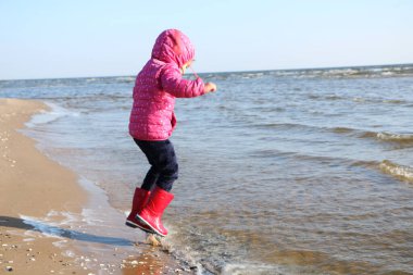 Sonbaharda deniz kenarında oynayan kız çocuğu. Deniz kıyısında güzel bir sonbaharda kırmızı ceketli bir kız. Kontrışık.