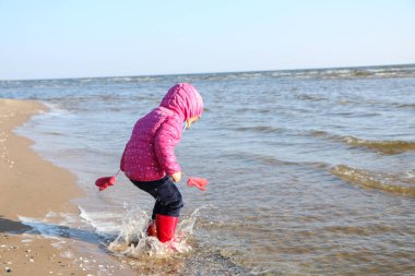 Sonbaharda deniz kenarında oynayan kız çocuğu. Deniz kıyısında güzel bir sonbaharda kırmızı ceketli bir kız. Kontrışık.