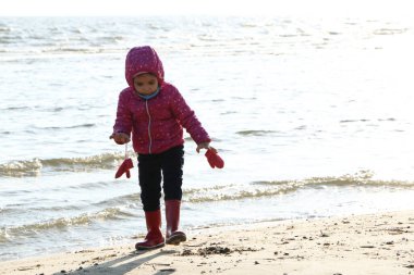 Sonbaharda deniz kenarında oynayan kız çocuğu. Deniz kıyısında güzel bir sonbaharda kırmızı ceketli bir kız. Kontrışık.