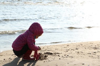 Sonbaharda deniz kenarında oynayan kız çocuğu. Deniz kıyısında güzel bir sonbaharda kırmızı ceketli bir kız. Kontrışık.