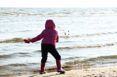 Sonbaharda deniz kenarında oynayan kız çocuğu. Deniz kıyısında güzel bir sonbaharda kırmızı ceketli bir kız. Kontrışık.