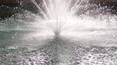 On a hot day, there is a beautiful fountain in the park. Splashes of water from the fountain in the backlight.