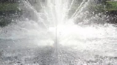 On a hot day, there is a beautiful fountain in the park. Splashes of water from the fountain in the backlight.