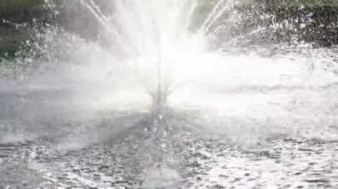 On a hot day, there is a beautiful fountain in the park. Splashes of water from the fountain in the backlight.