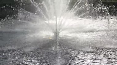 On a hot day, there is a beautiful fountain in the park. Splashes of water from the fountain in the backlight.