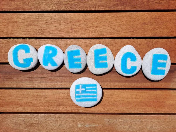 Greece country name painted on the stones on wooden plank background. Inskription on the sea stones.