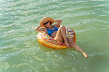 Dinlen. Bir kadın gölde şişme bir yüzüğün üzerinde yüzüyor..